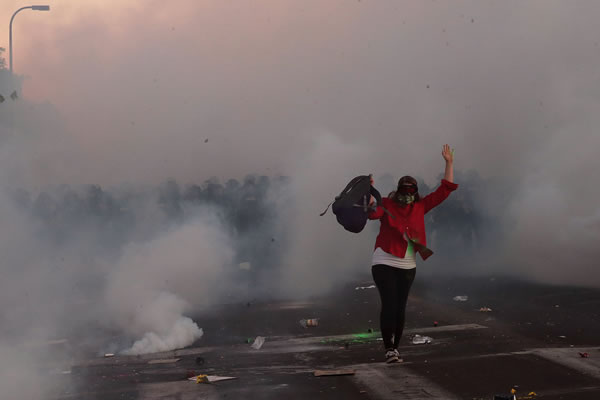 De entre todo el humo de los gases lanzados por la Policía sale una persona.